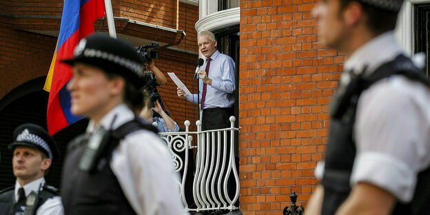 Ein Mann mit Mikrofon am offenen Fenster, vor ihm britische Polizisten