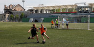 Zwei Jungen spielen Fußball im Zentralstadion von Irpin. Im Hintergrund eine Hausruine.