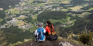 Zwei Personen sitzen nebeneinander auf einem Hügel und blicken in Täler hinab