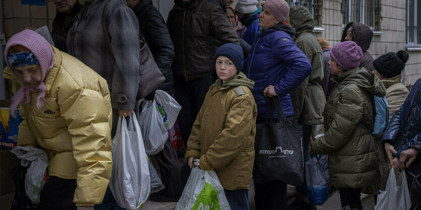 Menschen mit Tüten und Taschen in einer Schlange