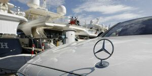 Ein Mercedes-Stern auf einer Kühlerhaube, im Hintergrund eine Yacht