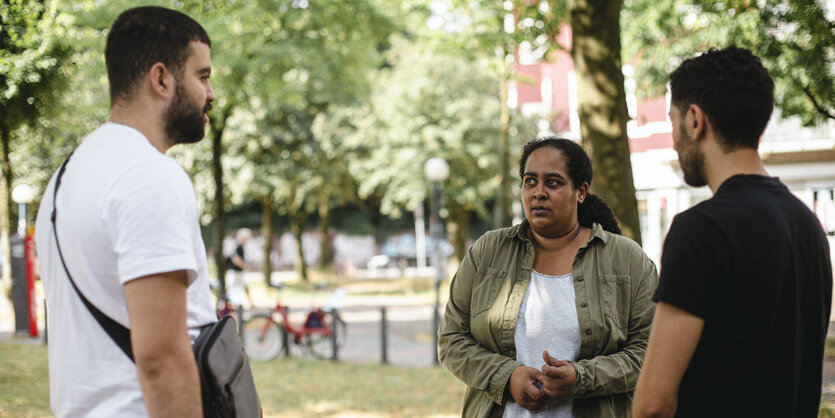 Unter einem Baum spricht eine Frau mit zwei Männern