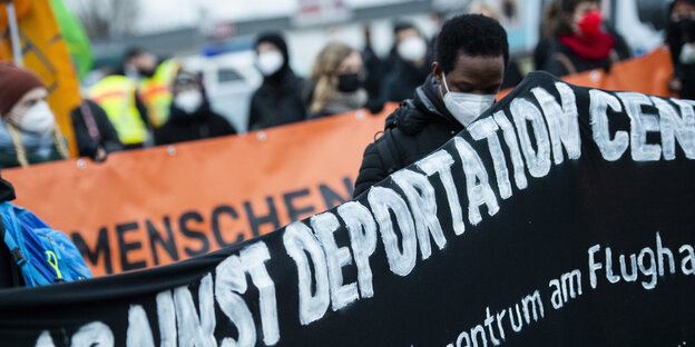 Ein Demonstrant in Schönefeld hinter einem Banner mit der Aufschrift Against Deportation Center.