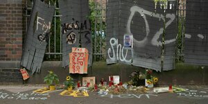 Tatort in Dortmund: Vor einem ramponierten Blechsichtschutz stehen Kerzen, Blumen und Fotos von Mouhamed D.