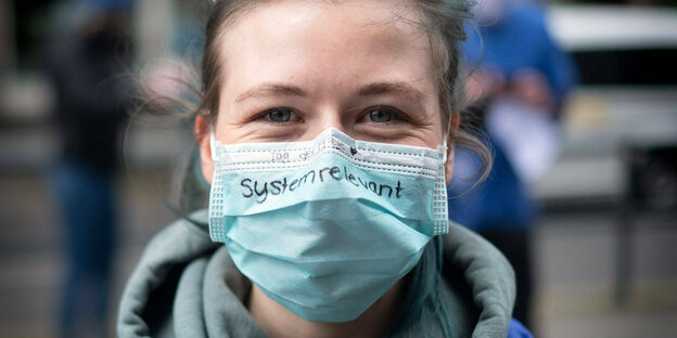 Eine Frau mit Maske, darauf die Aufschrift: "systemrelevant"