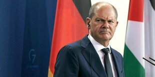 Olaf Scholz sitzt mit Knopf im Ohr vor einer Deutschlandflagge während der Pressekonferenz am 16. August