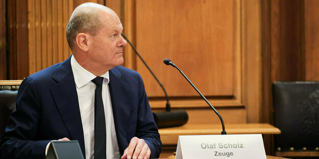 Olaf Scholz sitzt im Zeugenstand, vor ihm ein Mikrofon und ein Platzkärtchen: Olaf Scholz. Zeuge.
