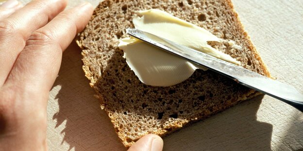 Eine Hand schmiert Butter auf eine Brotscheibe