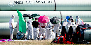 Menschen beim Protest in Maleranzügen vor einem Stapel von Pipeline-Rohren.