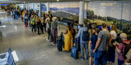 Menschen mit Reisegepäck stehen an einem Flughafen in einer langen Schlange.