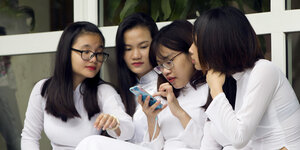 Vier junge Frauen sitzen auf einer Treppe und schauen gemeinsam in ein Smartphone
