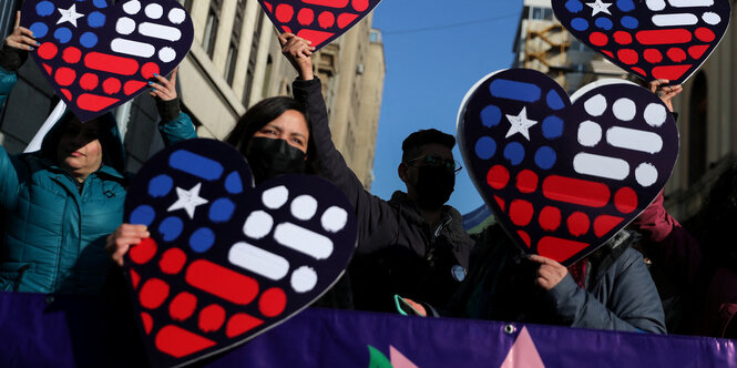 Demonstrant*innen halten Schilder in Herzform und den Nationalfarben Chiles hoch