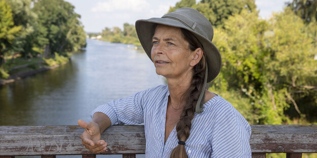 Frauke Bennett steht mit Hut auf einer Brücke über den Oder Podern, sie hat einen langen Zopf