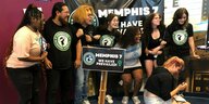 Eine Reihe junger Leute steht lachend zusammen, vor ihnen ein Schild "Memphis 7 - wir haben gewonnen!"