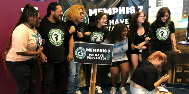 Eine Reihe junger Leute steht lachend zusammen, vor ihnen ein Schild "Memphis 7 - wir haben gewonnen!"