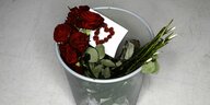 ein Strauß Rosen und eine Karte mit Rosenblüten-Herz liegen im Mülleimer