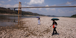 Zwei Menschen mit Regenschirmen als Sonnenschutz stehen auf weißen Steinen am Ufer eines Flusses