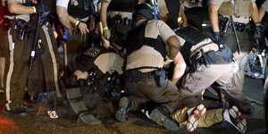 Polizisten in Uniform umringen und sitzen auf einem Protestierenden