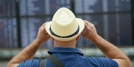Ein Mann mit Strohhut schaut auf die Informationstafel am Flughafen