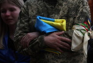 Ein Mann in Uniform verschränkt die Arme, er hält eine ukrianische Flagge