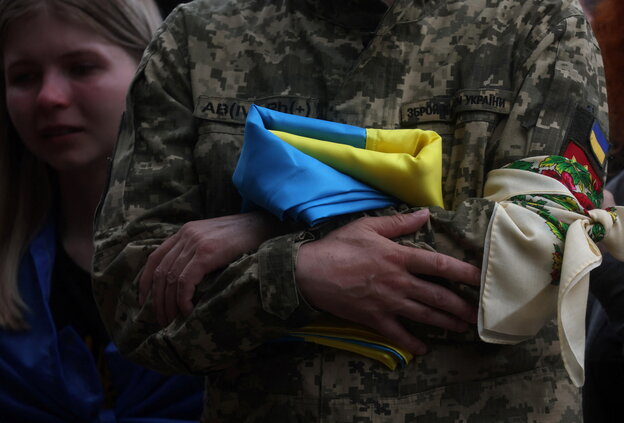Ein Mann in Uniform verschränkt die Arme, er hält eine ukrianische Flagge