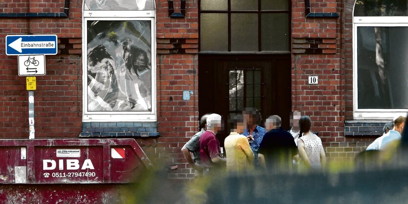 Eine Gruppe steht vor einem Backsteinhaus, die Gesichter sind verpixxelt