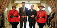 Olaf Scholz und Justin Trudeau stehen nebeneinander in einer Empfangshalle, flankiert von zwei rotuniformierten kanadischen Mounties
