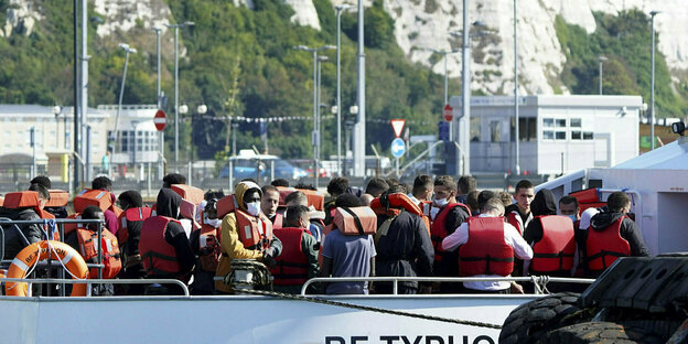 Eine Gruppe von Migranten steht mit Schwimmwesten in einem Boot das anlegt