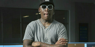 Dennis Rodman mit verschränkten Armen, Sonnenbrille und Basecap