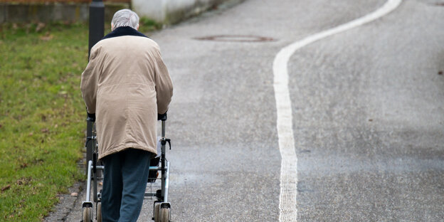 Eine ältere Frau geht mit einem Rollator auf einem Weg entlang.