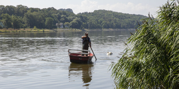 Ein Fischer rudert stehend in seinem Boot und zieht einen totoen Wels hinter sich her