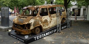 Das ausgebrannte Auto der Ausstellung "Testament von Butscha" neben einer Informationstafel.