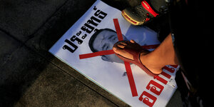 Zwei Protestierende treten auf ein Plakat mit dem Porträt von Prayut Chan-o-cha, das mit einem roten Kreuz versehen wurde