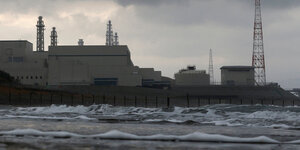 Atomkraftwerk im Hintergrund, Wellen und Strand im Vordergrund.