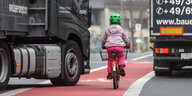 Ein kleines Mädchen fährt auf dem Fahrradweg zwischen zwei Lastwagen, einer der LKWs fährt bedrohlich auf den Radweg
