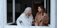 Eine ältere und eine junge Frau stehen am Fenster und reden miteinander, die Stimmung wirkt gestresst