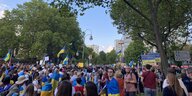 Zu sehen ist eine Menschenmasse von mehreren Hundert Leuten. Sie demonstrieren und haben fast alle eine ukrainische Flagge in den Farben blau und gelb um die Schultern.