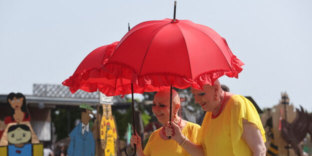 Zwei Menschen mit jeweils einem roten Sonnenschirmchen an der Hand auf der Documenta 2022 in Kassel