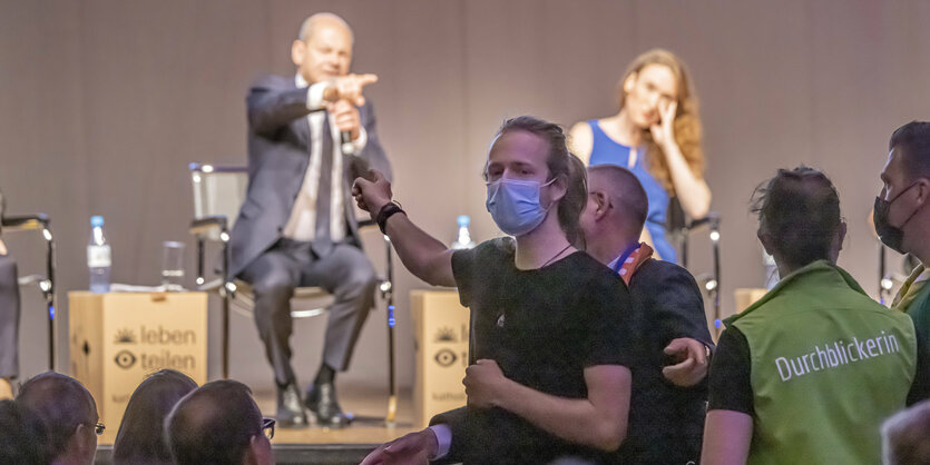 Aktivist:innen protestieren bei einer Podiumsdiskussion mit Bundeskanzler Scholz.