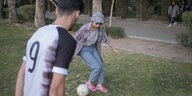 Ein Mann und eine Frau speilen in einem Park Fußball.