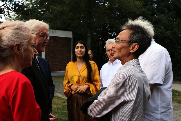 Izabela Tiberiade steht mit Frank Walter Steinmeier während einer gedenkveranstaltung in Rostock in einer Gruppe mit anderen Menschen zusammen