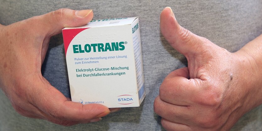 Eine Hand hält eine Packung mit dem Durchafllmittel Elotrans, die andere Hand zeigt den gehobenen Daumen