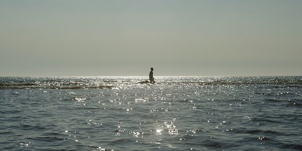 A lonely person stands in the wide sea at sunset