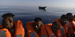 Migranten in Rettungswesten vor einer Wasser-Kulisse