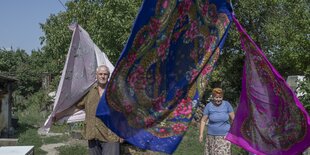 Ein älteres Ehepaar steht unter der mit bunten Tüchern behangenen Wäscheleine in ihrem Garten. Der liegt gegenüber dem AKW Saporischschja