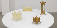 Auf einem runden Tisch stehen vier Skulpturen von Aleksandra Kasuba. Die Skulpturen sind aus aufgespannten Stoffen, sie fügen sich zu organische Formen mit Spitzen zusammen und zum Teil vergoldet.