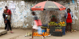 Eine Frau verkauft Früchte unter einem Sonnenschirm mit dem logo der regierungspartei