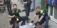 Zwei Polizisten knien auf einem Mann, einer hat einen Taser gezogen, ein Polizist im Hintergrund hat eine Schusswaffe in der Hand