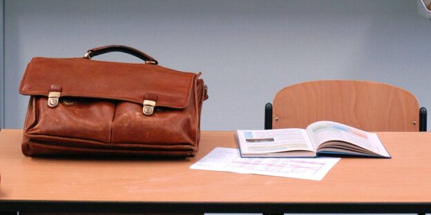 A briefcase and an open textbook lie on a desk