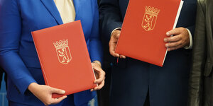 2 rote Mappen mit Berlin-Siegel werden von den Händen Franziska Giffey und Andreas Geisels gehalten
